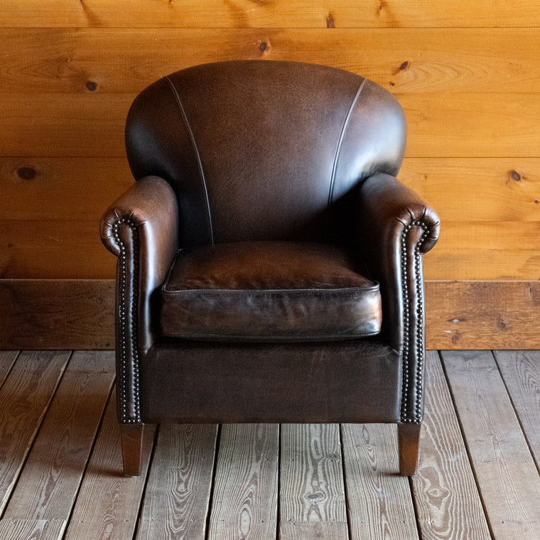 Back view of a tight back rustic arm chair with nailhead trim against a wooden wall 