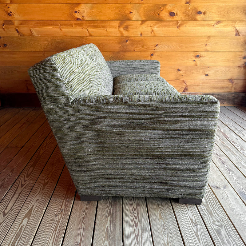 Profile view of an 88" tight-back sofa upholstered in a mossy, mottled fabric against a wooden wall