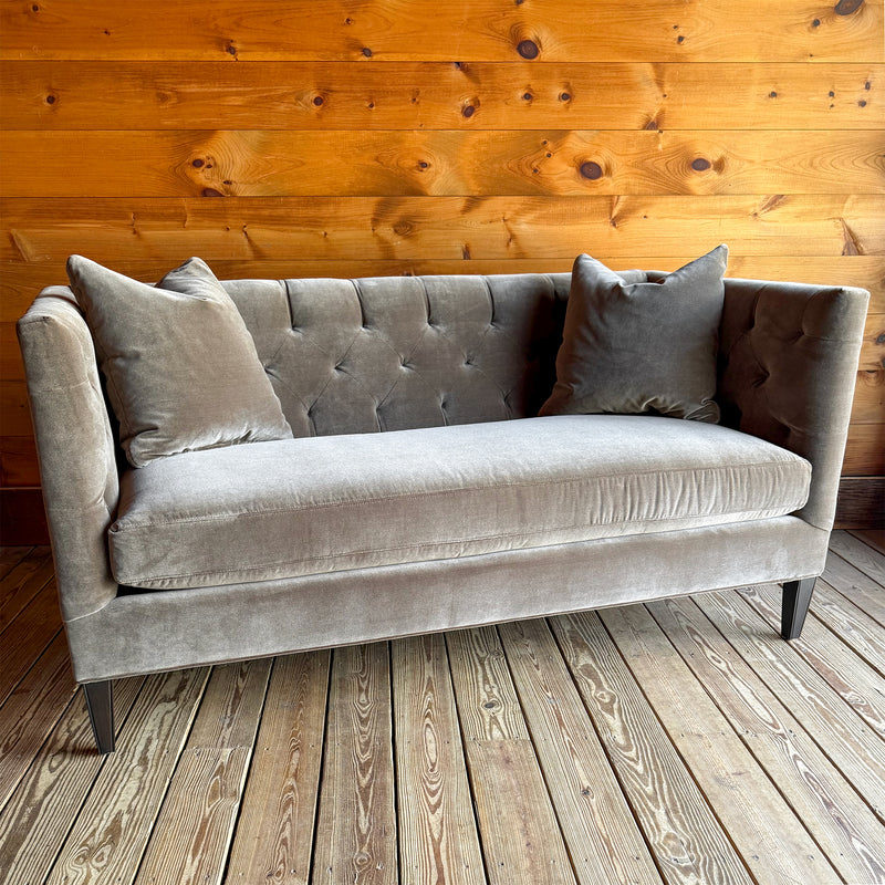 Angled front view of a brown-gray velvet tufted shelter arm sofa on a wooden floor against a wooden wall