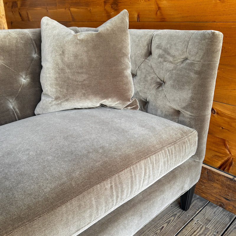 Close-up of the arm of a brown-gray velvet tufted shelter arm sofa and pillow against a wooden wall