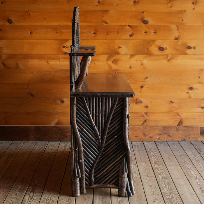 Profile view of an Adirondack style twig mosaic sideboard with hidden storage, a gallery, mirror, and display shelves on a wide plank wooden floor against a rustic wooden wall