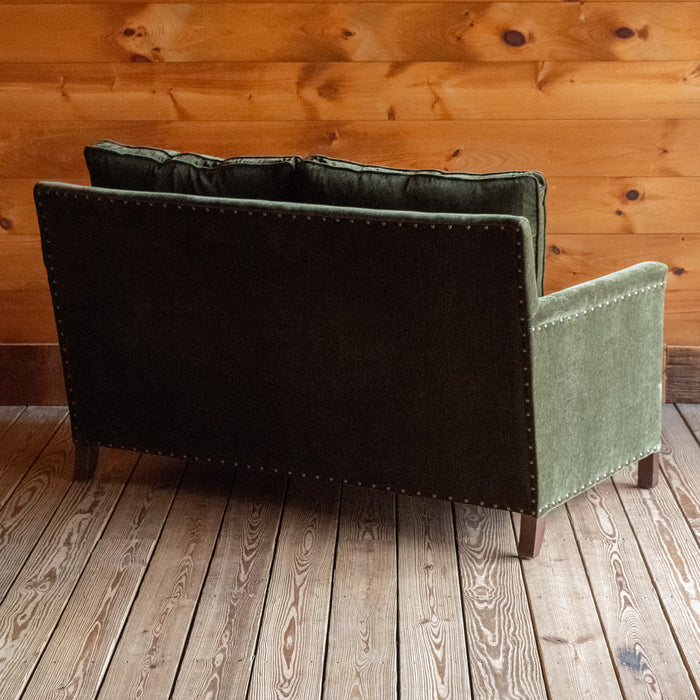 Loose back loveseat upholstered in a green velvet fabric with track arms and nailhead trim, Angled back view