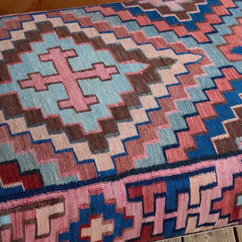 Close-up of a vintage rug covered ottoman in shades of blue, rust, cream, and brown