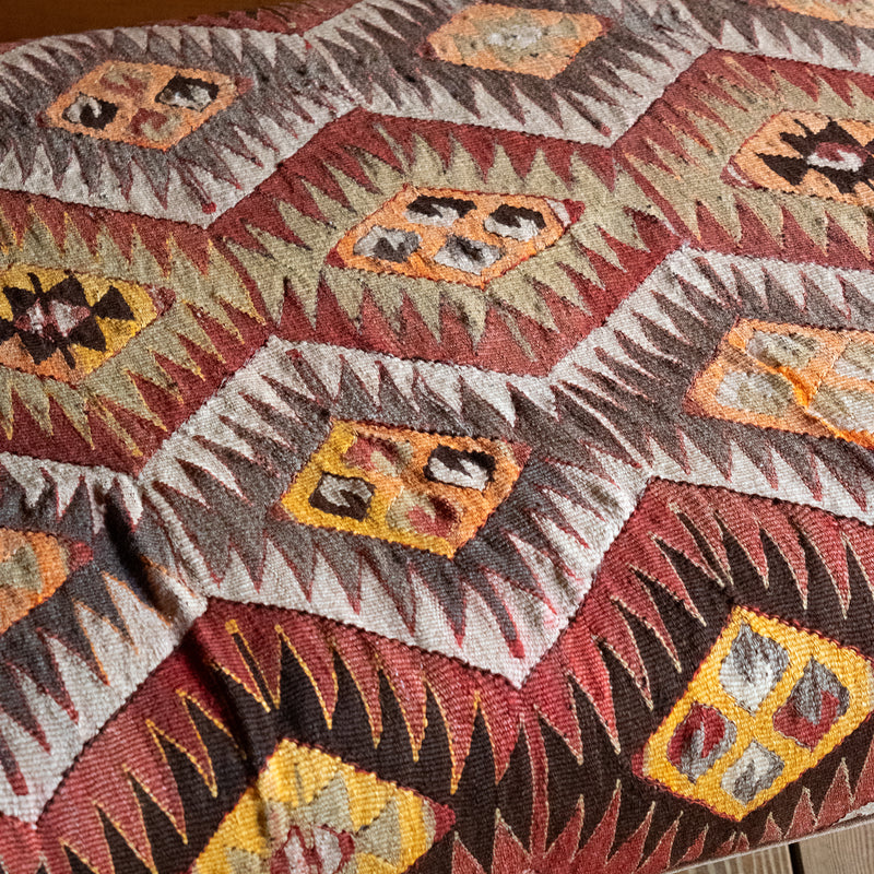 Close-up of a vintage rug covered ottoman in shades of rust, green, cream, and brown