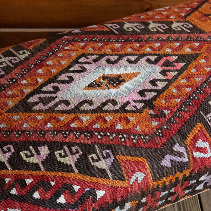 Close-up of a vintage rug covered ottoman in shades of red, orange, cream, and brown