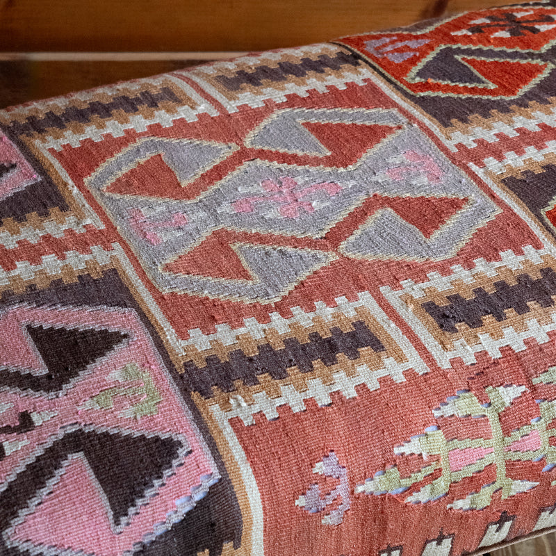 Close-up of a vintage rug covered ottoman in shades of rust, green, cream, and brown