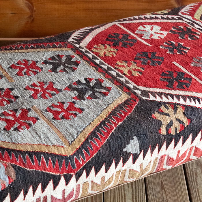 Close-up of a vintage rug covered ottoman in shades of red, blue, cream, and brown