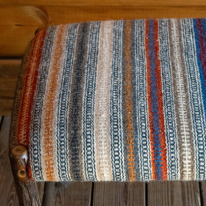 Close-up of the seat of a rustic hickory bench upholstered in a striped wool fabric